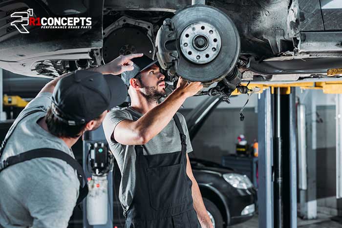 Mechanice inspecting brake parts on vehicle